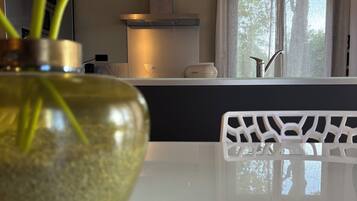 Une cuisine moderne avec un plan de travail blanc, un vase contenant des plantes vertes et des luminaires suspendus.