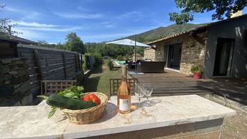 Un espace patio avec un plan de travail en pierre, un panier en osier rempli de légumes, une bouteille de vin et deux verres.