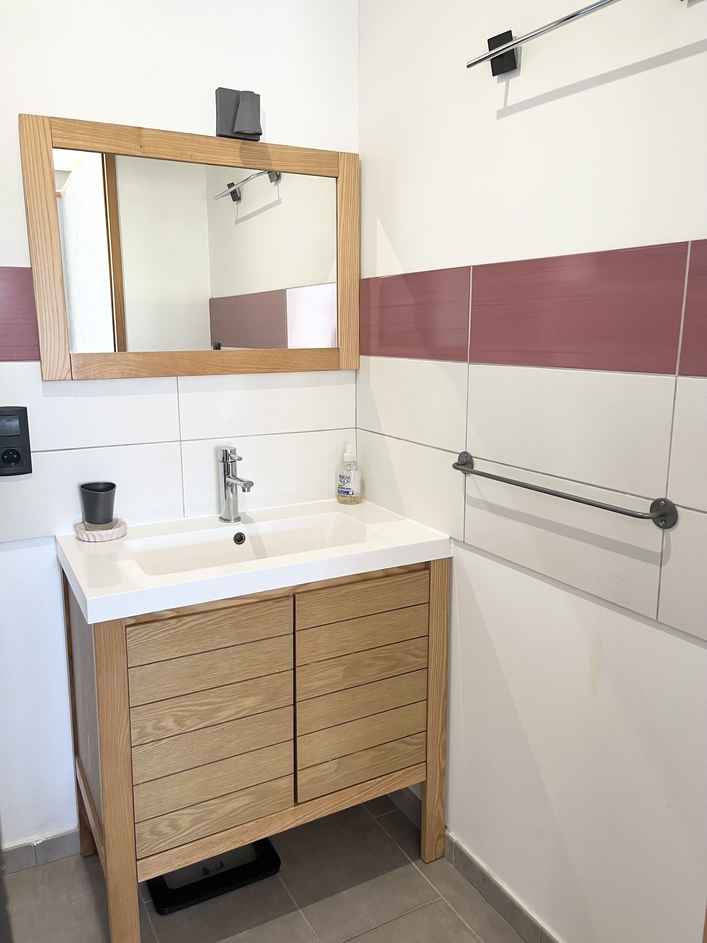 A bathroom with a wooden vanity, a mirror, a white sink, and a towel rack.