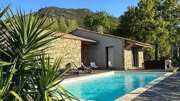 Un espace piscine agrémenté d’un bâtiment en pierre, de chaises longues et d’une terrasse en bois.