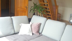 Un saló amb un sofà seccional gris, una catifa vermella amb dibuixos, una escala de fusta i una porta que dona a una altra habitació.