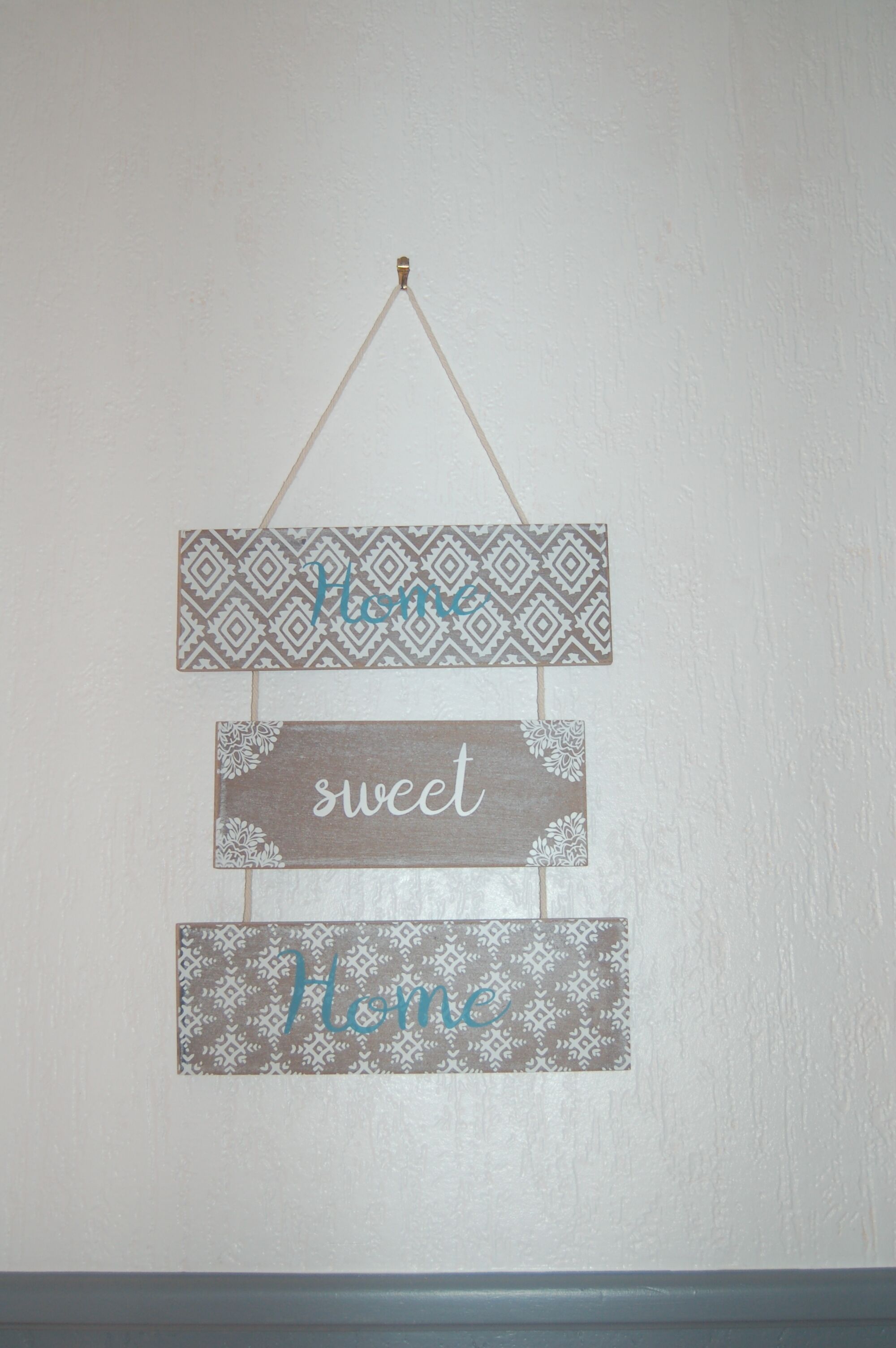 Un letrero montado en la pared con tres paneles de madera, cada uno con un diseño diferente y la palabra 'Home' escrita en ellos.