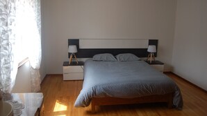 Un dormitori amb un llit, taules de nit, làmpades i una finestra amb cortines.