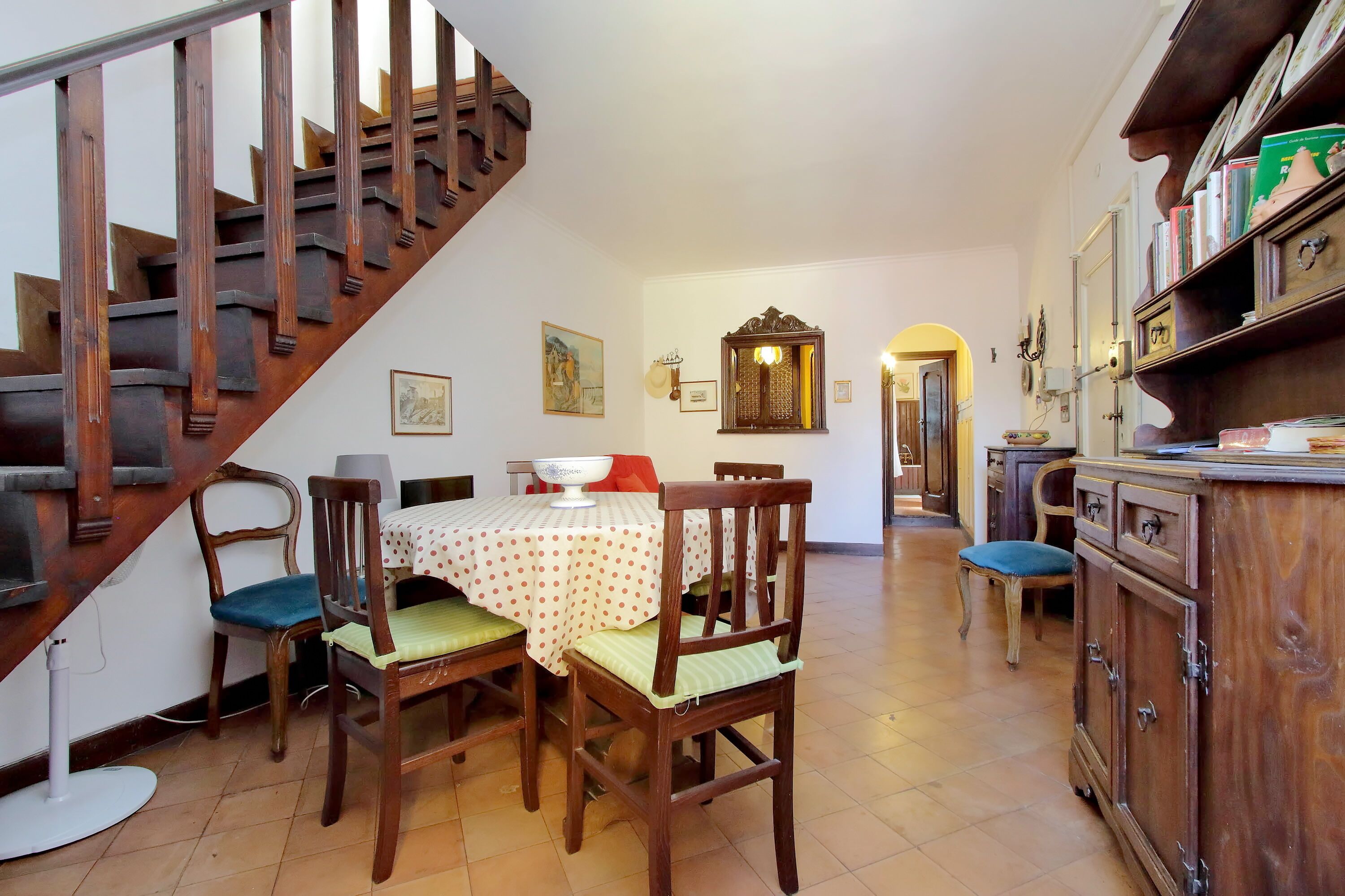 A dining area with a wooden staircase, a dining table with chairs, and a cabinet with dishes.