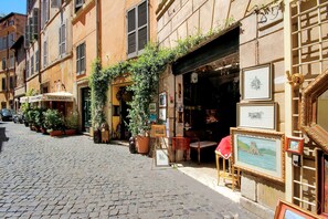 A cobblestone street with a restaurant named "Ristorante" on the left, featuring outdoor seating and potted plants.