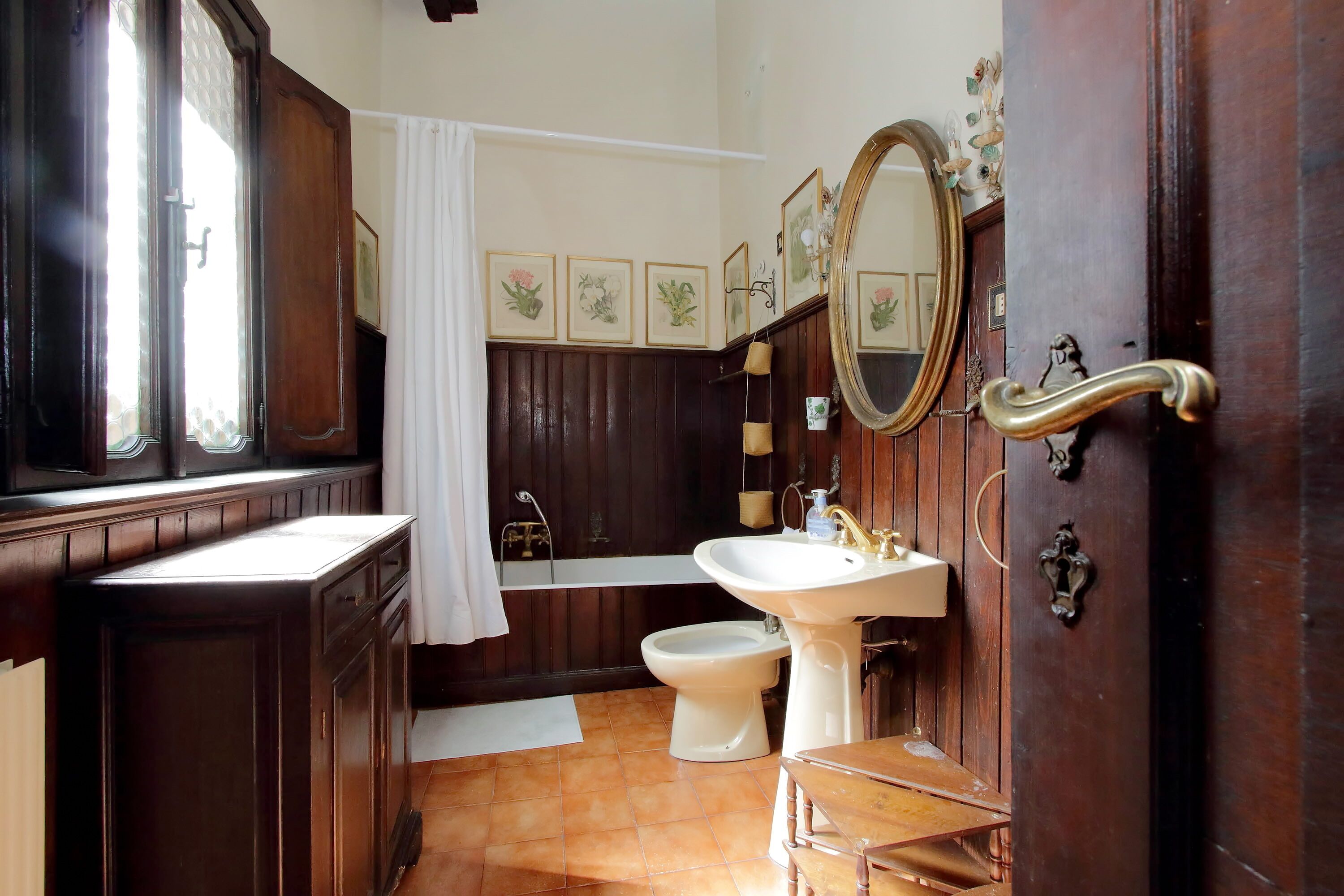 A traditional bathroom with a wooden vanity, a pedestal sink, a toilet, and a large mirror.