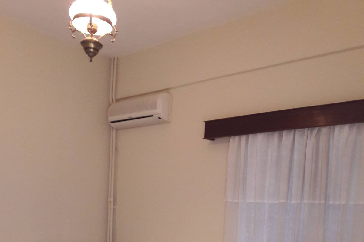Habitación de hotel con cama, mesita de noche, cómoda, equipo de aire acondicionado y ventana con cortinas.