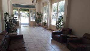 A spacious lobby with a tiled floor, leather sofas, potted plants, and large windows offering a view of the outside. - Nestor (Zacharo)