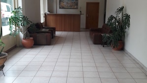 A reception area with a tiled floor, potted plants, a wooden reception desk, and a painting on the wall. - Nestor (Zacharo)