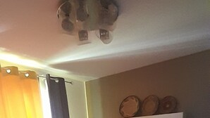 A hotel room with a bed, curtains, a shelf with decorative items, and a ceiling light fixture. - Villa close to the beach (Aimargues)