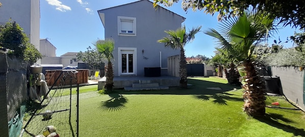 A modern two-story house with a well-maintained lawn, a small patio, and a few palm trees.