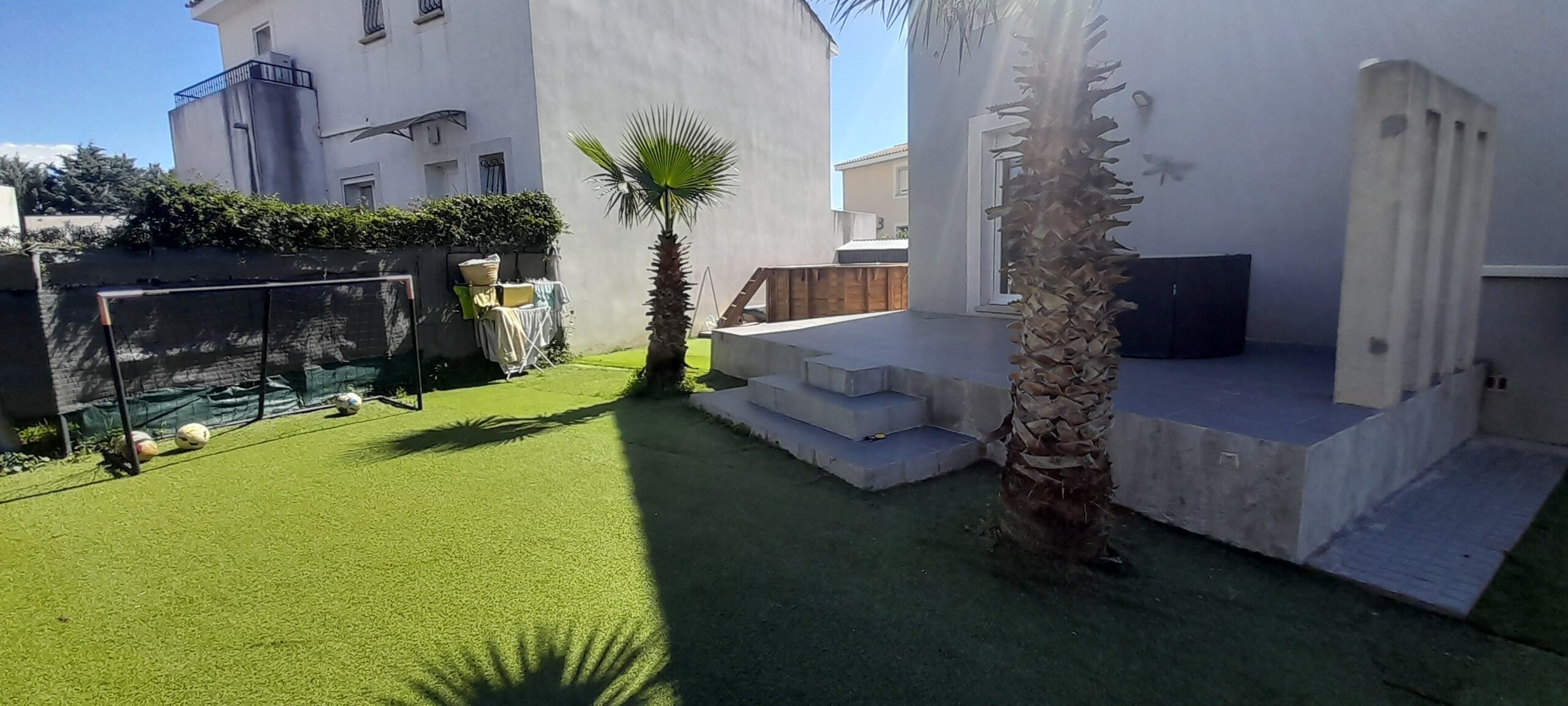 A courtyard with artificial grass, palm trees, and a concrete bench.