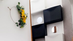 A staircase with dark steps and a wooden handrail. There is a wall-mounted shelf with a black object and a circular mirror. A floral wreath hangs on the wall to the left. - Villa close to the beach (Aimargues)