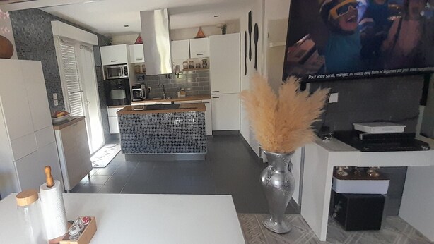 A modern kitchen with white cabinets, a central island, and a dining area with a white table. - Villa close to the beach (Aimargues)
