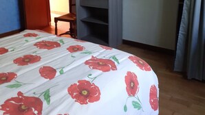 A bedroom with a bed covered in a floral bedspread, a wardrobe, and a chair.