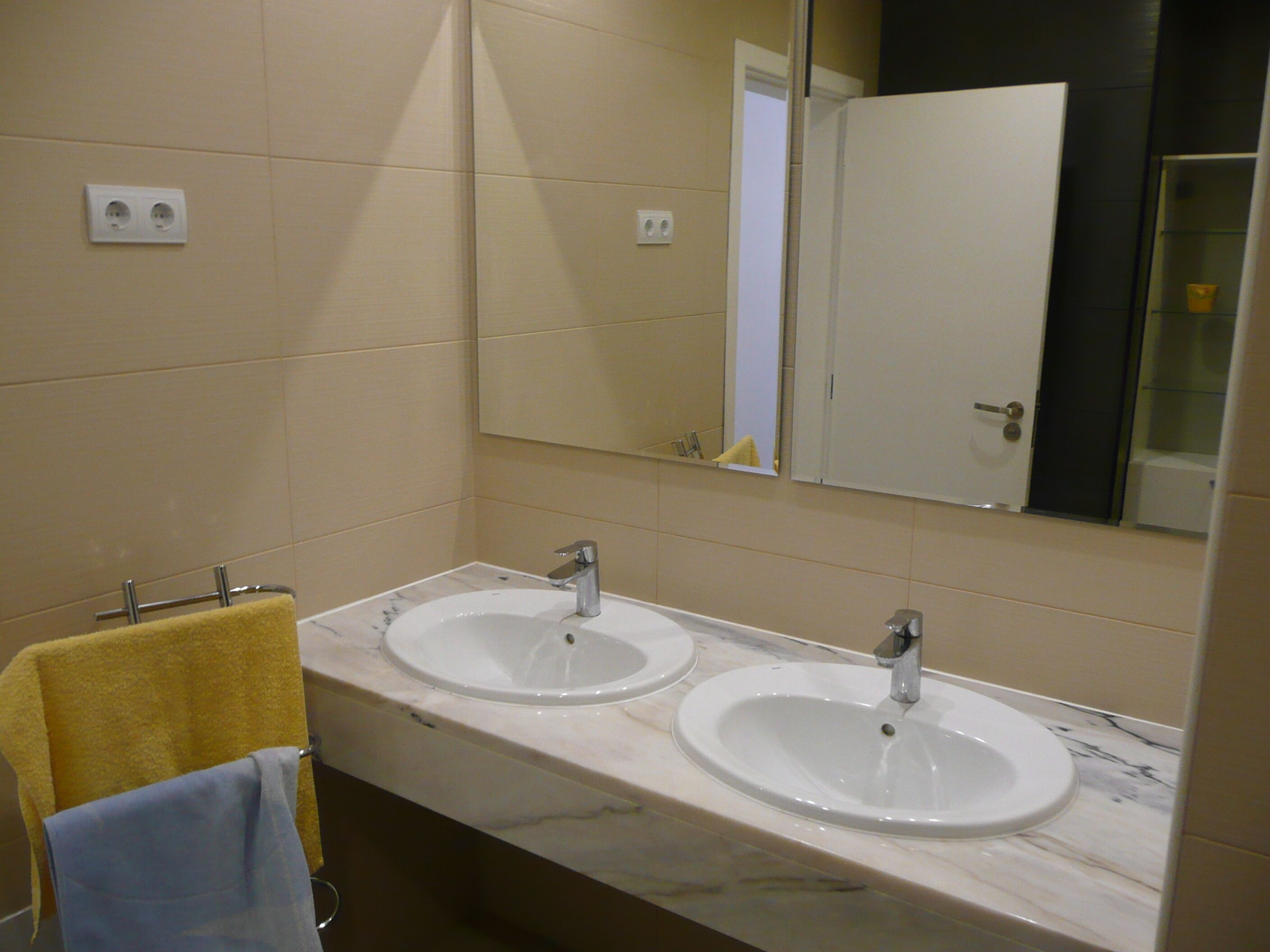 Une salle de bain avec deux lavabos, un miroir et un porte-serviettes avec des serviettes jaunes et bleues.