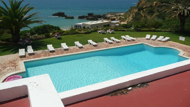 A pool with white lounge chairs and a view of the ocean.