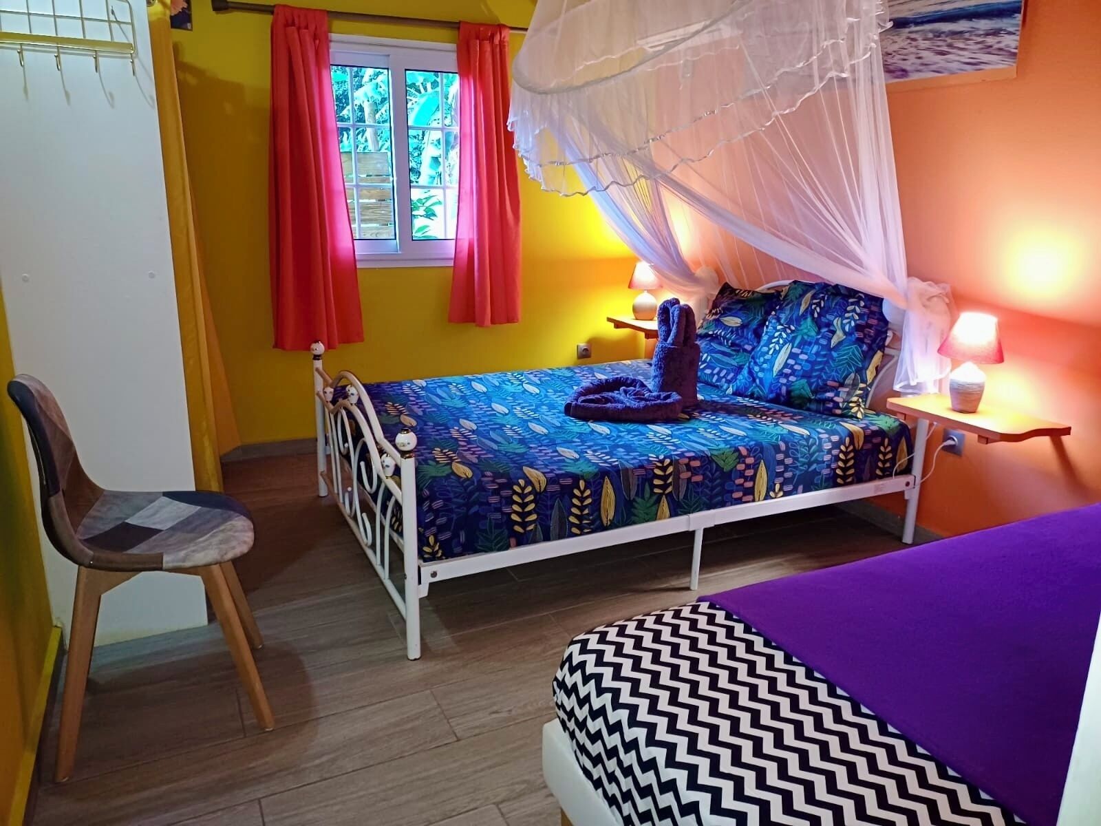 A bedroom with a bed, a chair, a bedside table with a lamp, and a window with curtains.