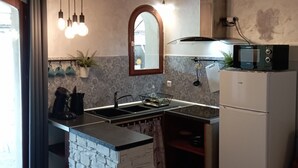 Cocina con una isla central, estufa integrada, microondas y refrigerador. Hay una ventana con cortinas, una lámpara colgante y un salpicadero de azulejos.