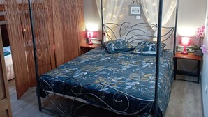 Una cama con dosel adornada con una colcha floral, dos lámparas de noche y una pequeña orquídea en maceta sobre la mesita.