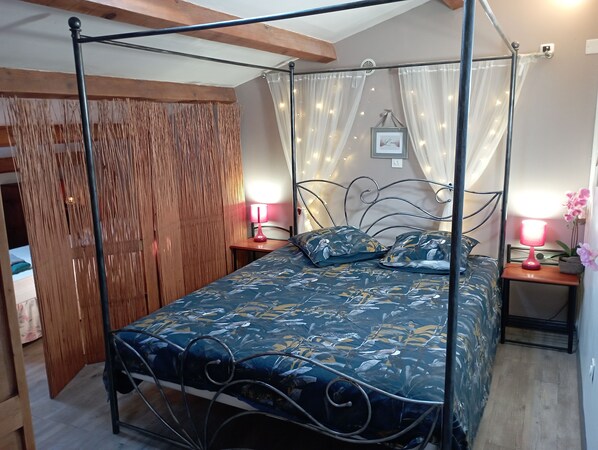 Una cama con dosel adornada con una colcha floral, dos lámparas de noche y una pequeña orquídea en maceta sobre la mesita.