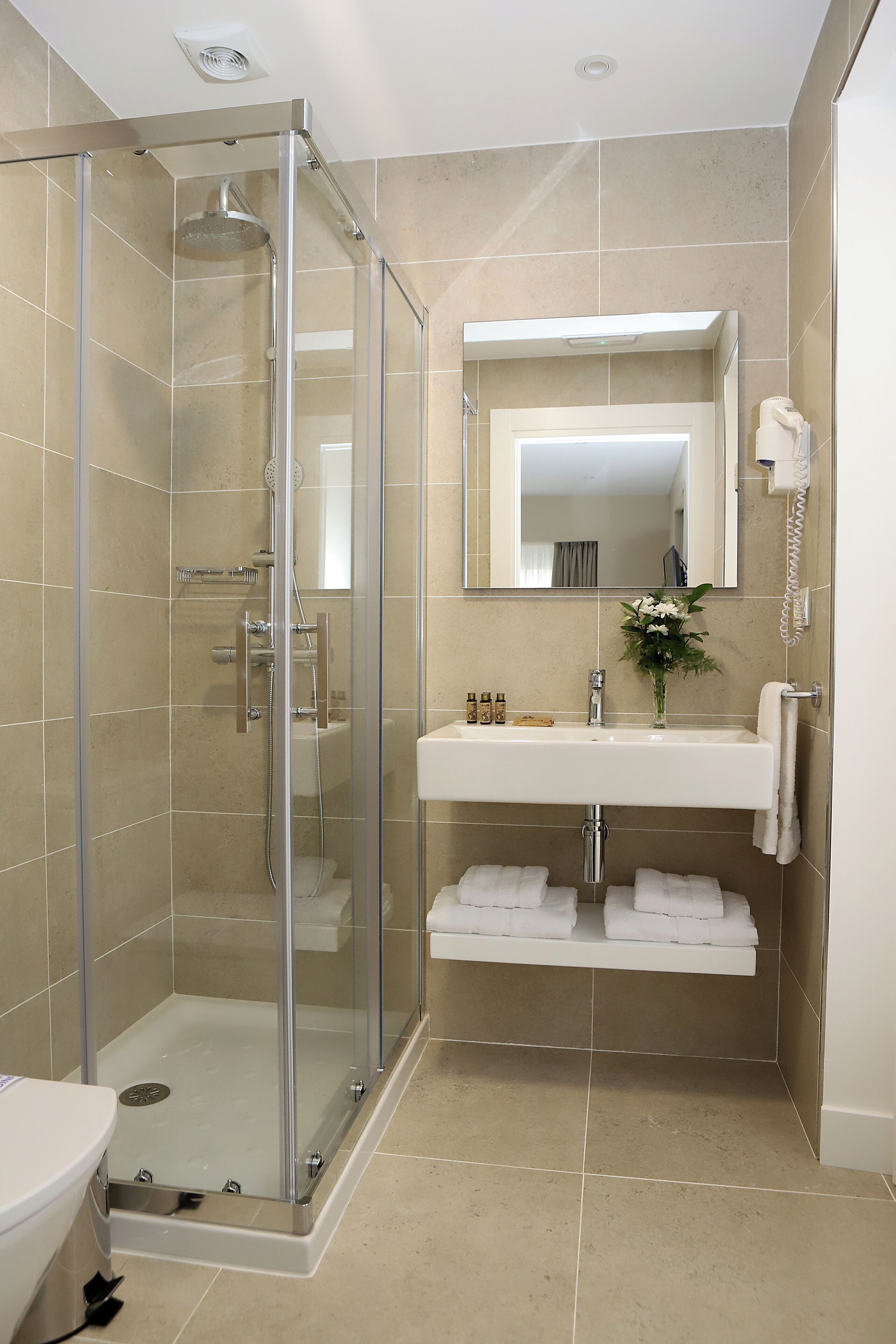 A modern bathroom with a glass-enclosed shower, a white sink with a mirror above, and a towel rack.