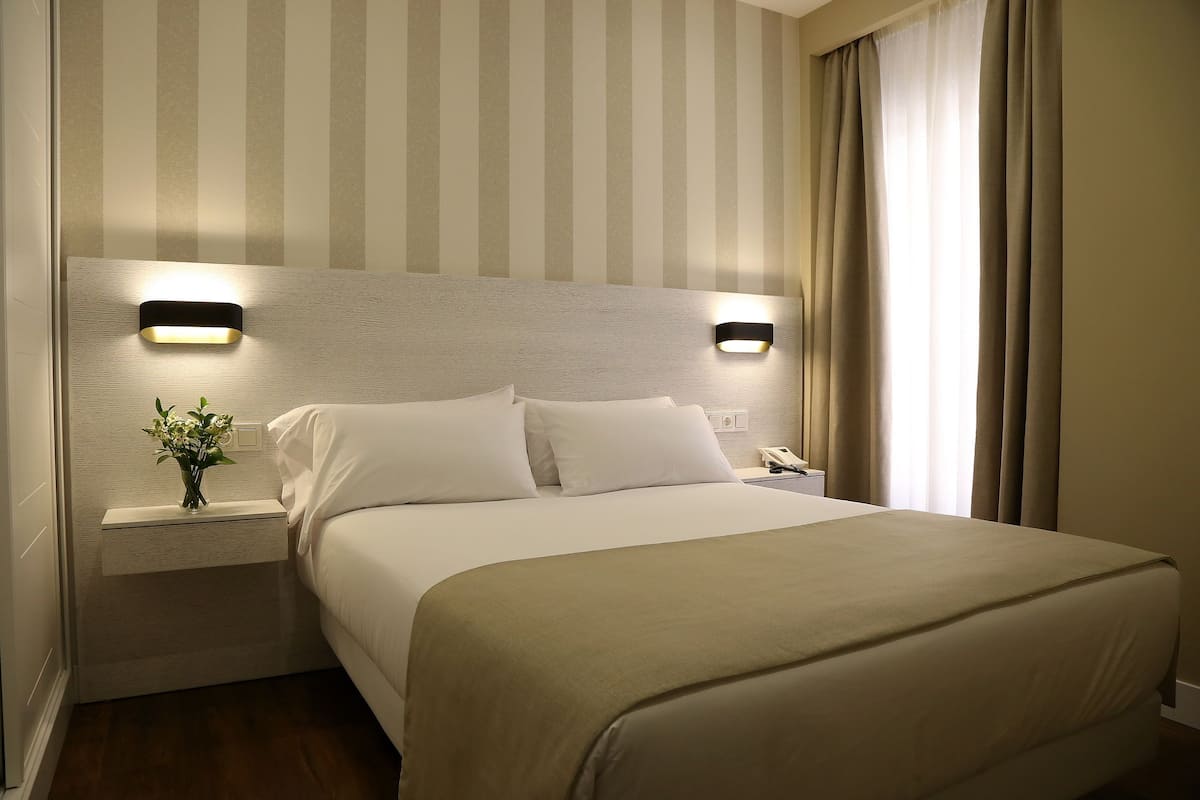 A neatly made bed with a beige bedspread, two bedside tables with lamps, and a striped wallpaper background.