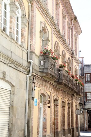 A historic building with arched windows and a balcony with flower boxes. - Vía XIX (Caldas de Reis)