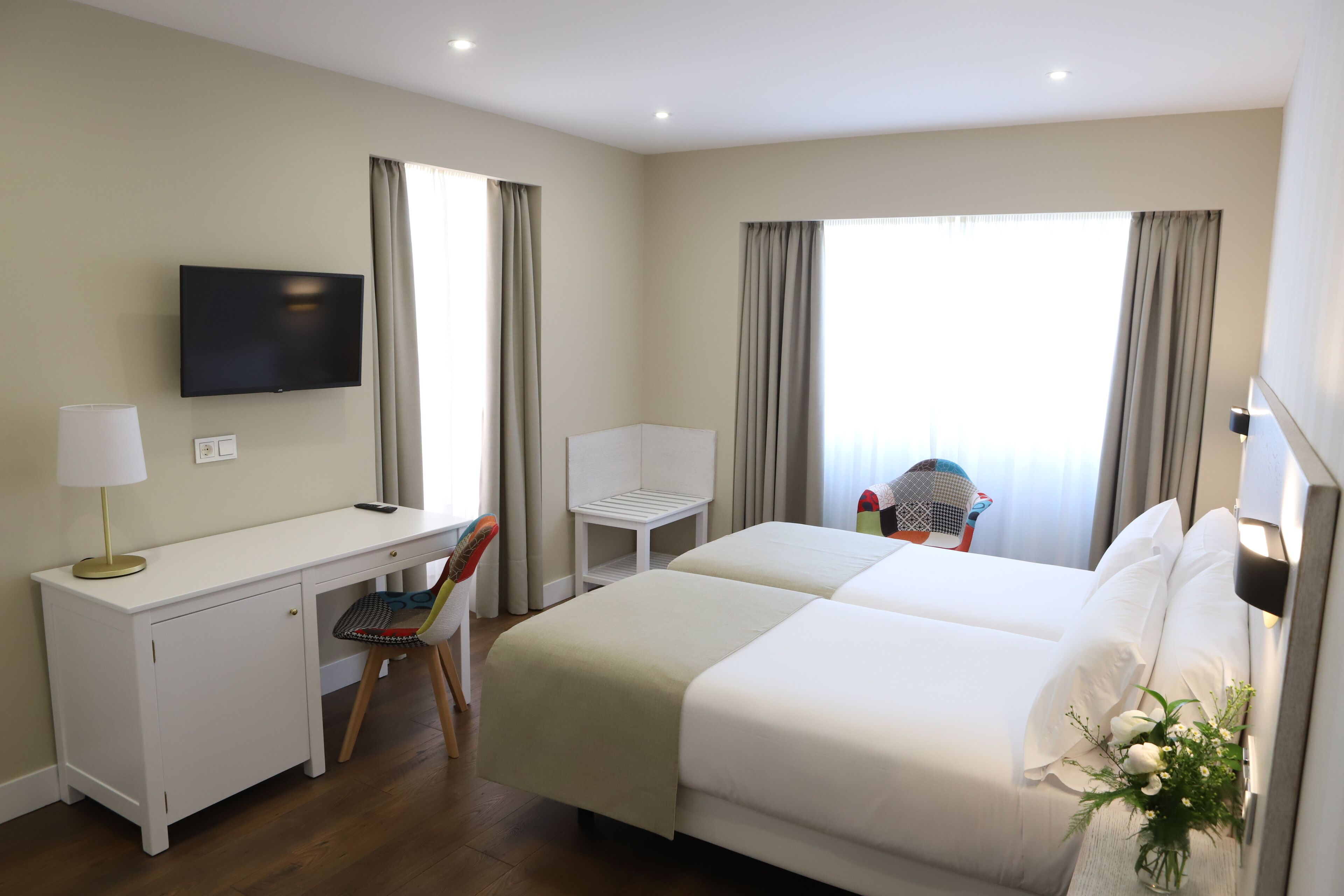 A hotel room with a bed, desk, chair, TV, and curtains.