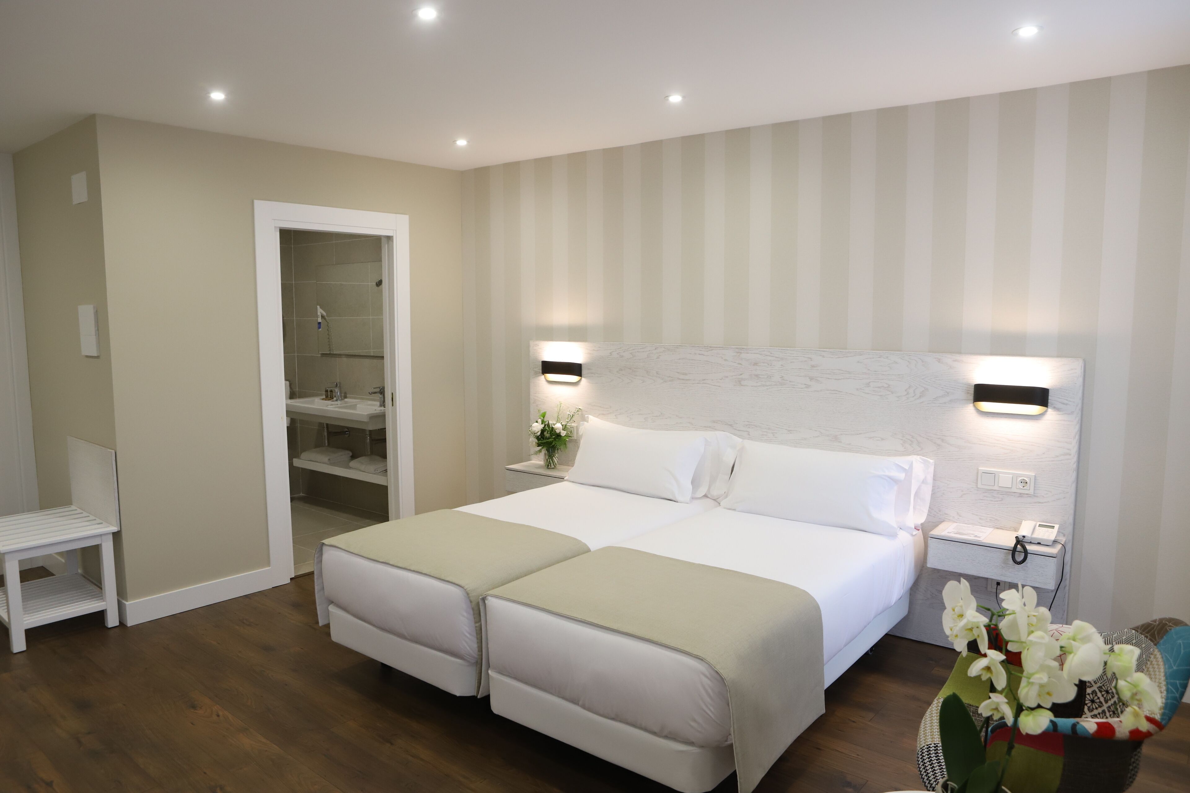 Cama doble con cabecera, mesitas de noche, una pequeña zona de estar y un baño con ducha.