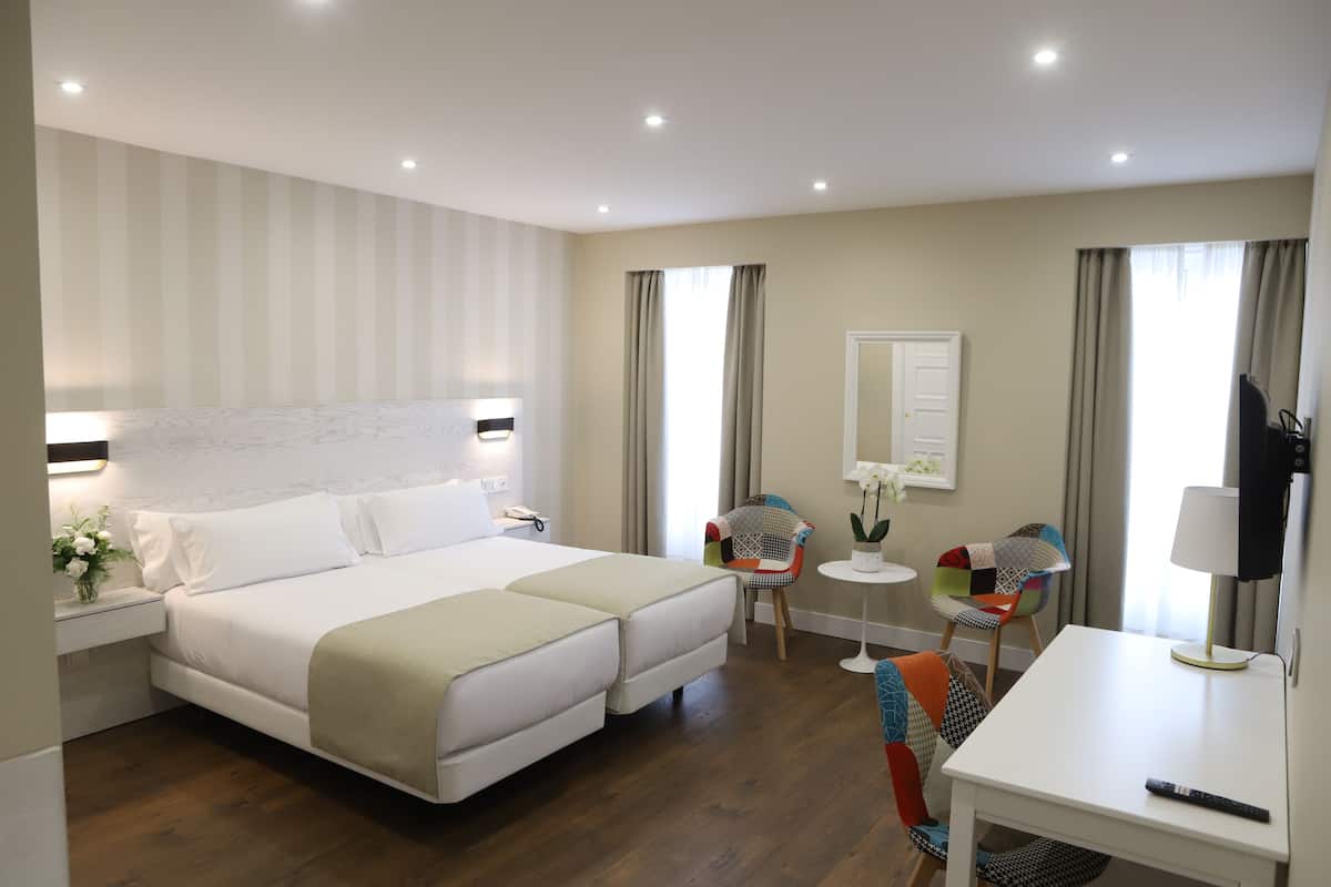 A hotel room with a large bed, two chairs, a desk, and a mirror.