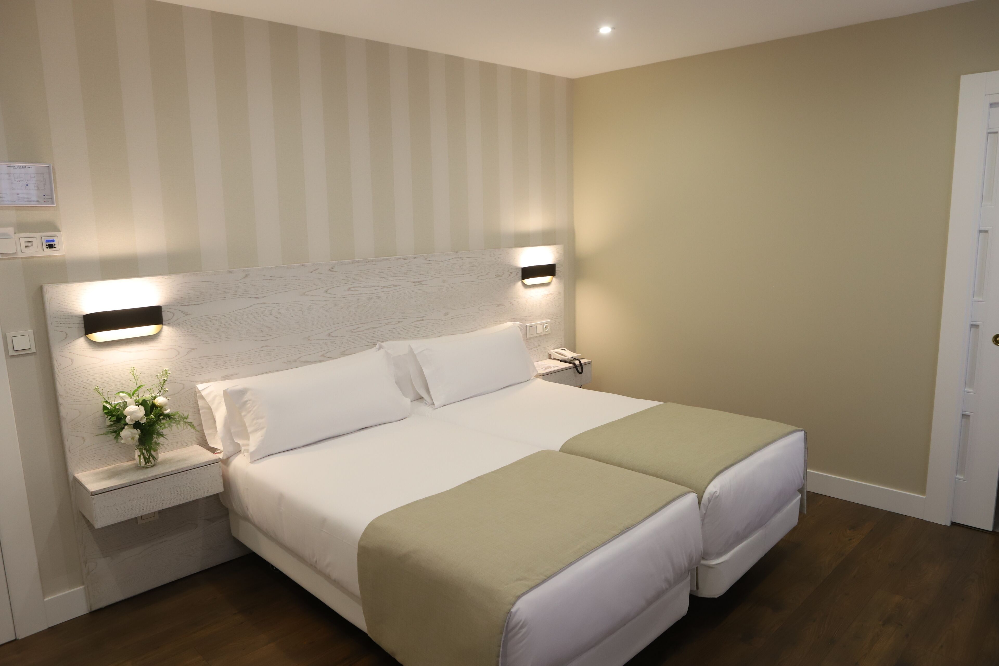 Una cama doble con dos almohadas, una mesita de noche con lámpara y un aplique de pared.