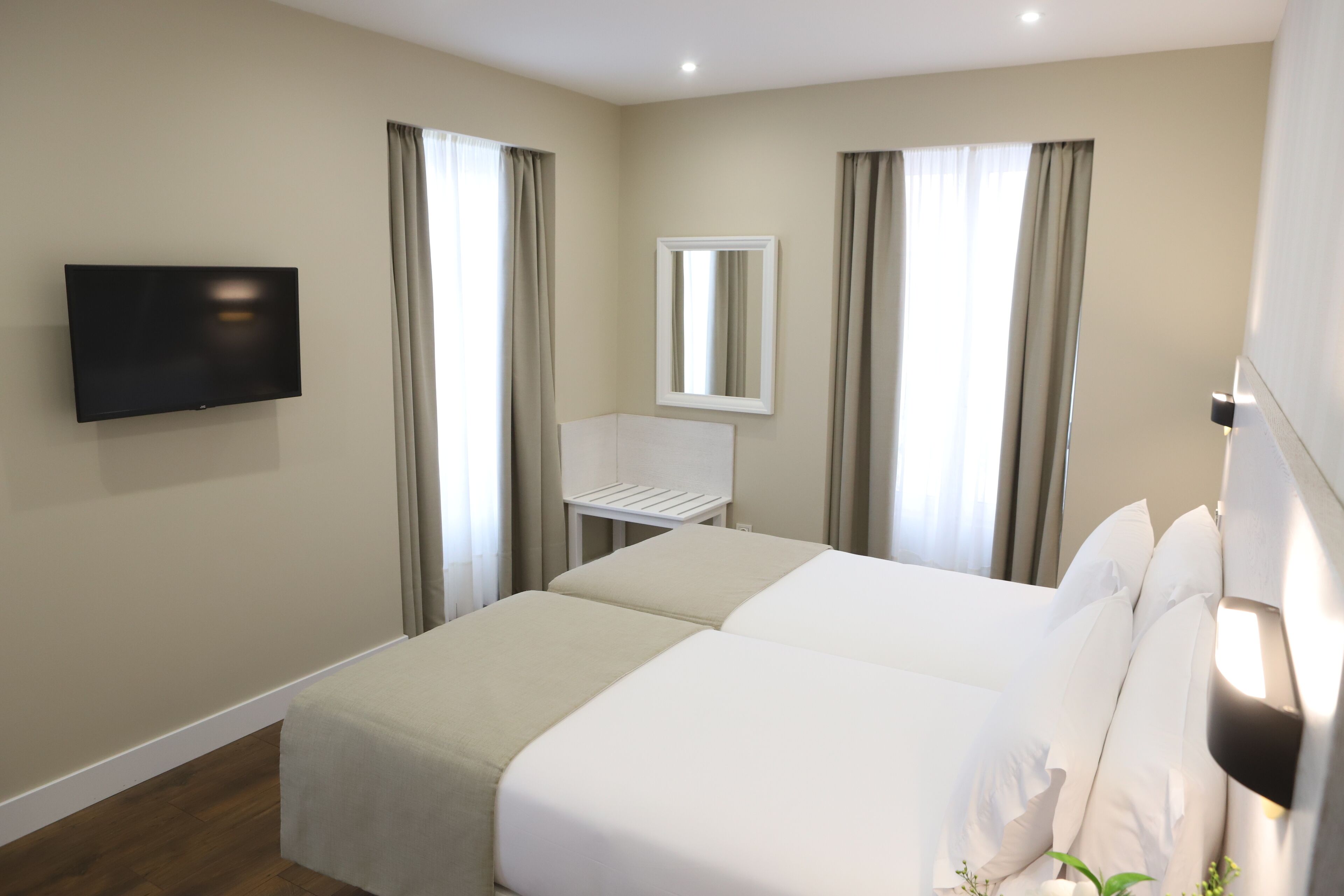A hotel room with two beds, a TV mounted on the wall, a small table, and a mirror.