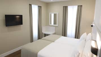 A hotel room with two beds, a TV mounted on the wall, a small table, and a mirror.