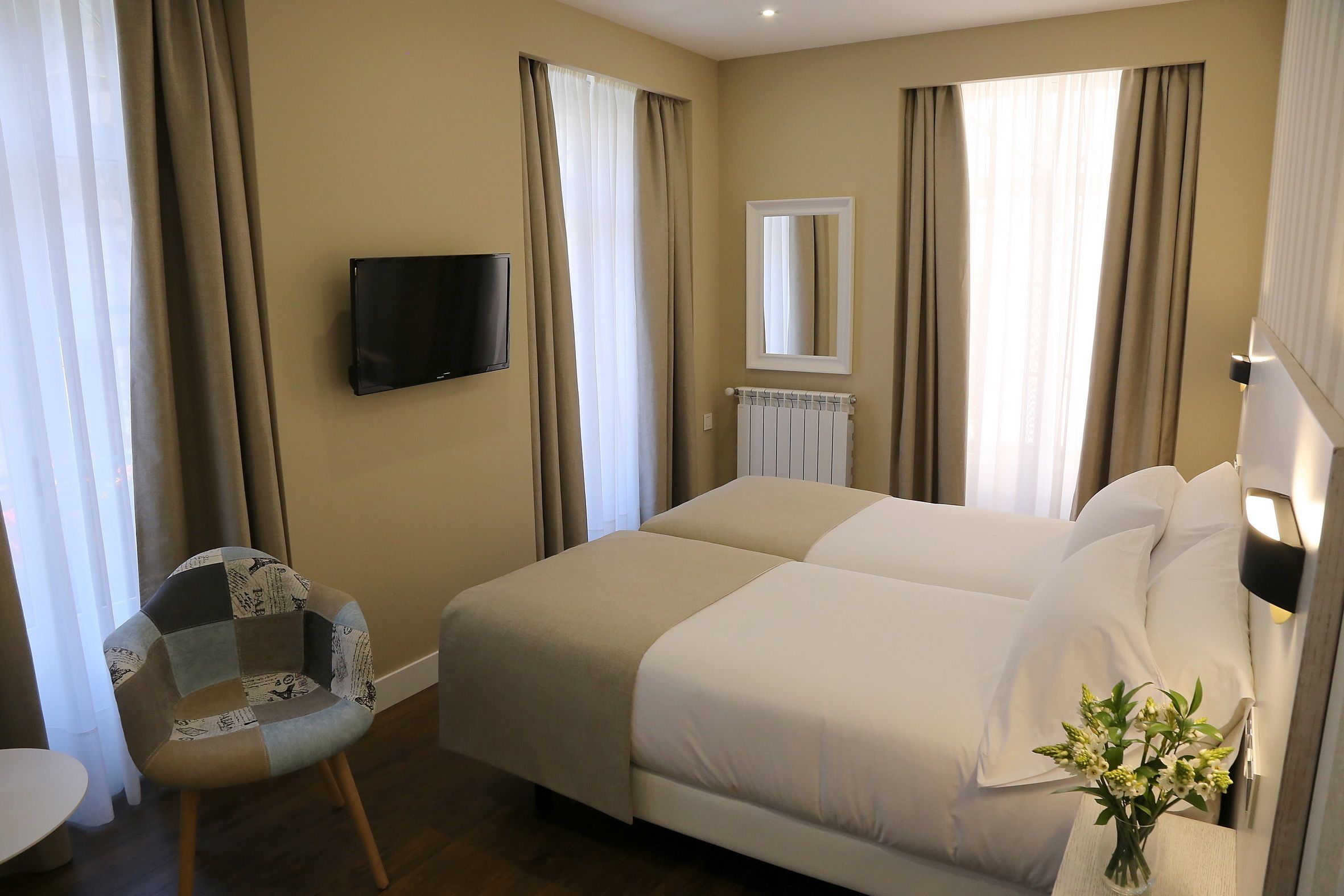 A hotel room with a large bed, a chair, a TV, and a vase with flowers.