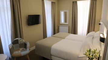 A hotel room with a large bed, a chair, a TV, and a vase with flowers.
