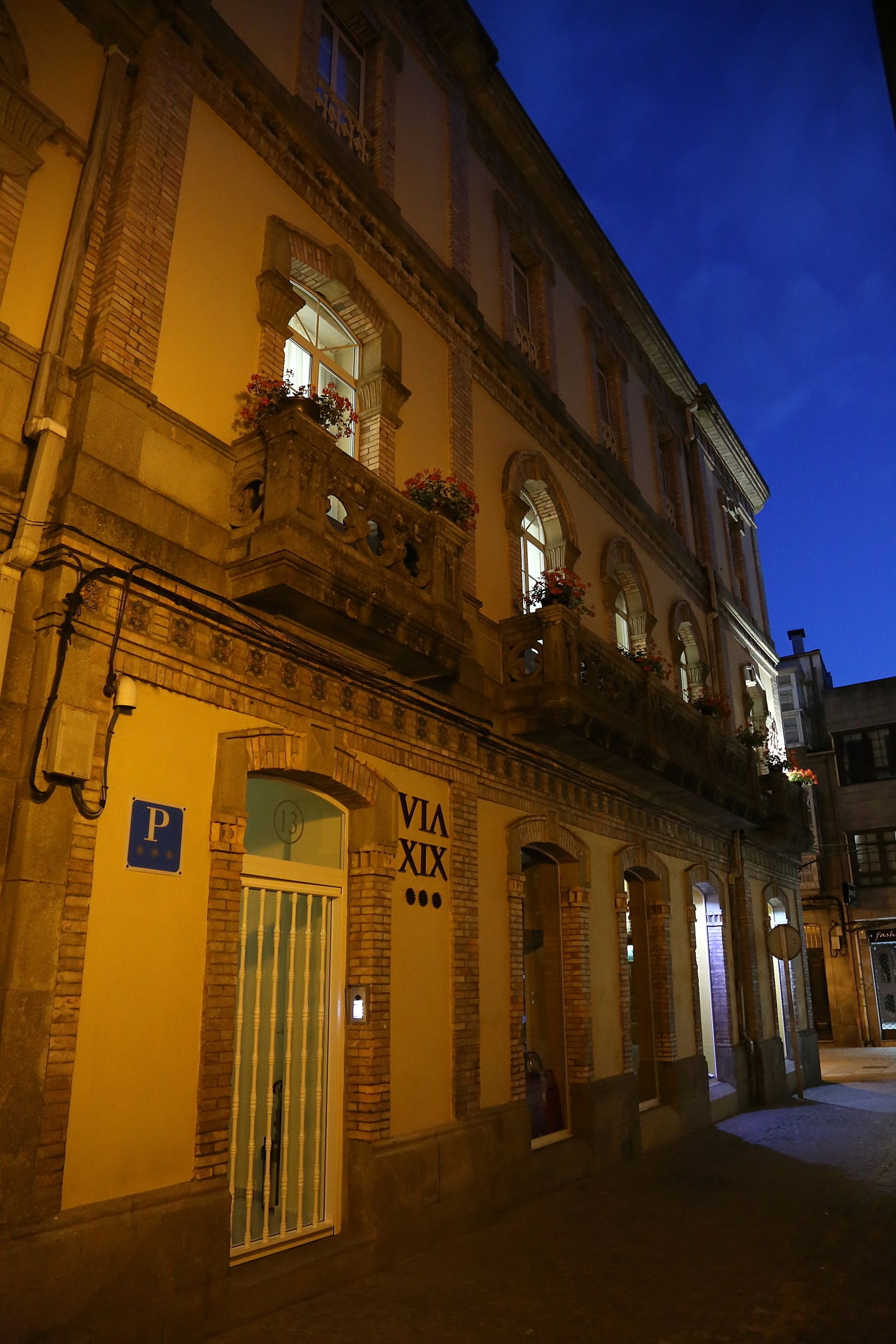 Un edificio histórico con un letrero que dice "VIA XIX" y un cartel de estacionamiento.
