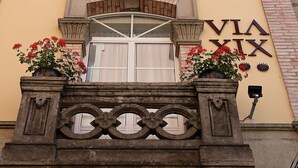 Fachada de edificio con un amplio ventanal de arco, un balcón con barandillas decorativas y un letrero con números romanos.