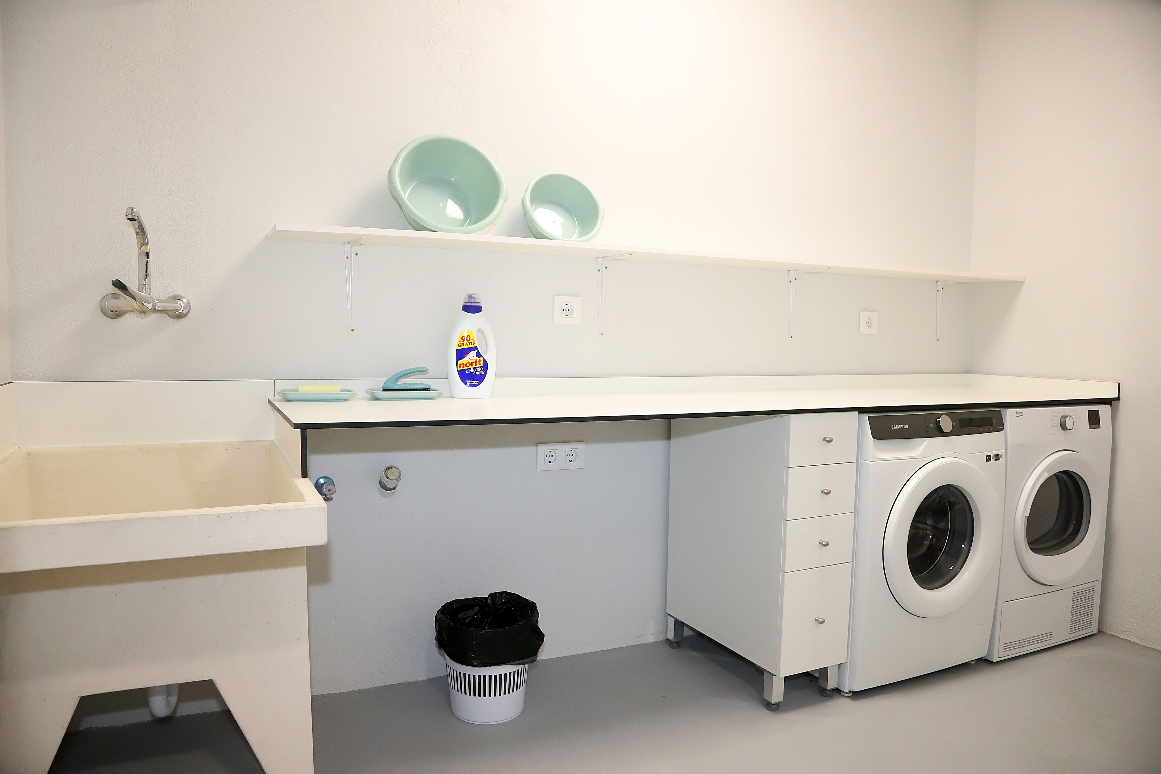 Un área de lavandería con lavadora, un lavabo y un bote de basura.