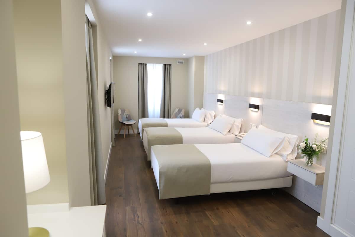 A hotel room with three beds, a desk, and a chair.