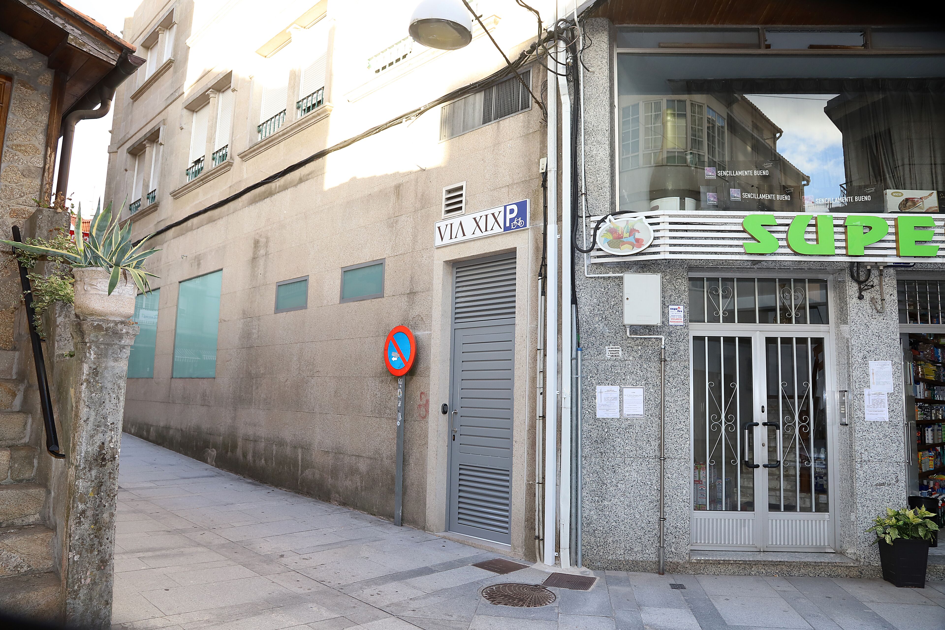 A building with a closed metal door, a no parking sign, and a storefront with a sign that reads "SUPER".
