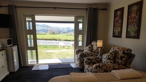 Ein Hotelzimmer mit Bett, Sofa, Fernseher und Blick auf eine grüne Landschaft durch die Tür.