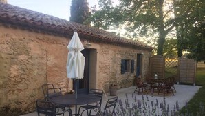 Patio esterno con tavolo rotondo e sedie, un ombrello bianco e una pianta in vaso.