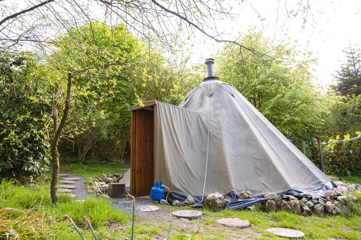 A tent with a chimney, surrounded by rocks and a path.