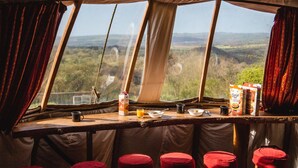 A cozy interior with a bar area, stools, and a view of the landscape through large windows. - Larkhill Tipis and Yurts (Llandysul)
