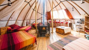 A cozy interior of a dome-shaped tent with two beds, a fireplace, and a small kitchen area. - Larkhill Tipis and Yurts (Llandysul)