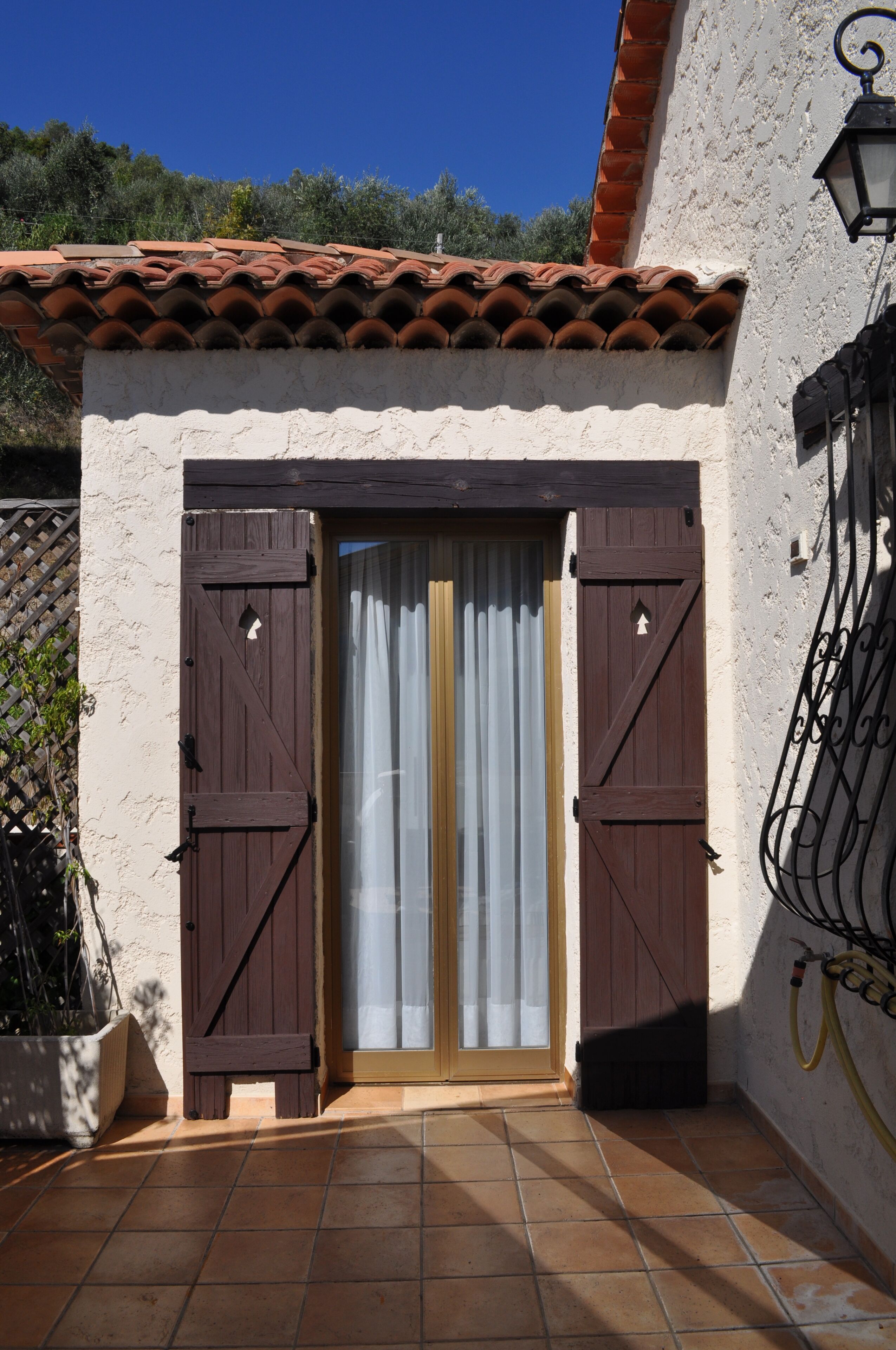 Una entrada de edificio con techo de tejas, pared blanca y puerta de madera con contraventanas.