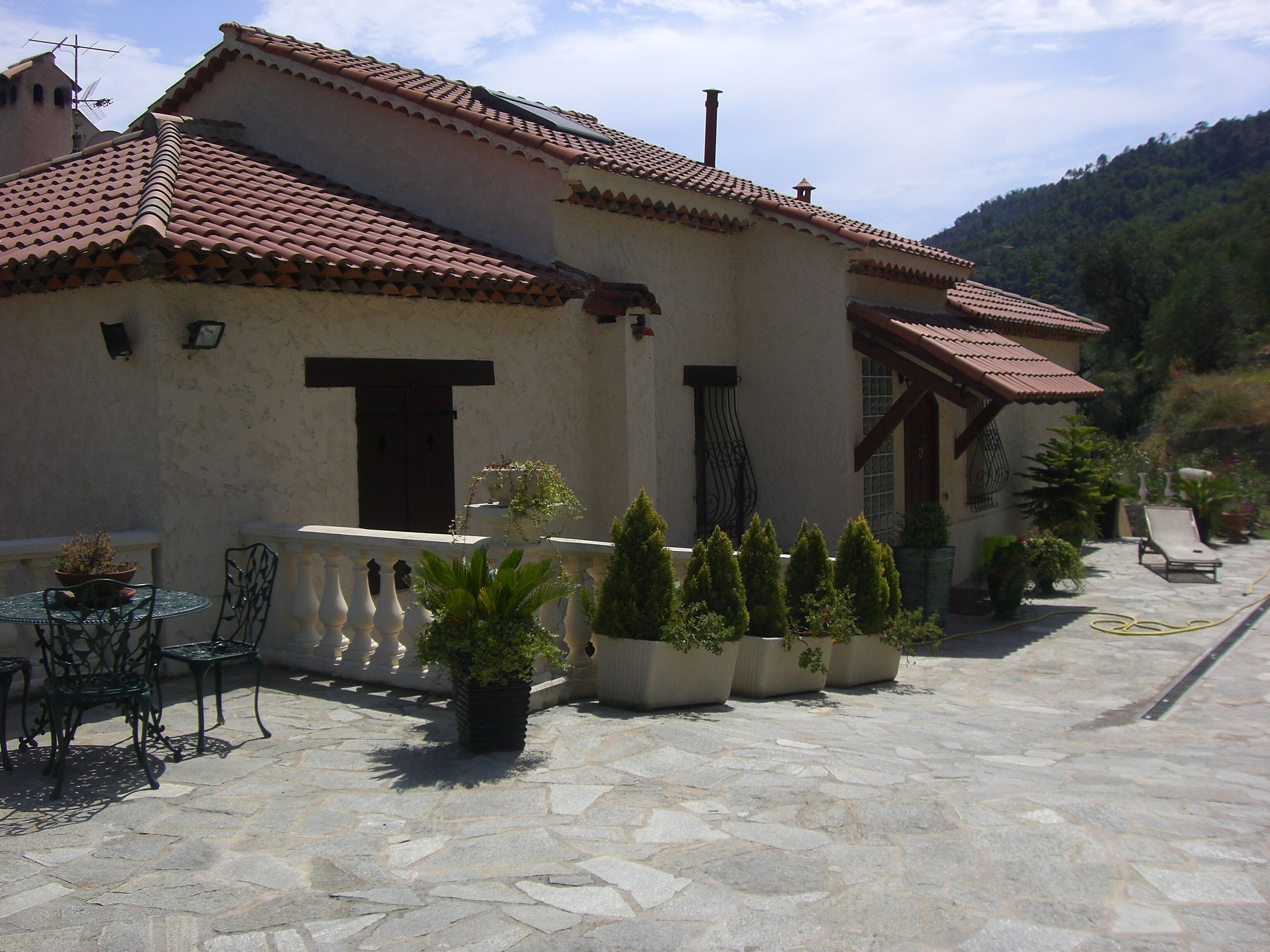 A building with a tiled roof, stone flooring, outdoor seating, and potted plants.