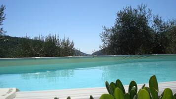Une piscine d’eau cristalline, entourée d’une végétation luxuriante, avec des collines en arrière-plan.