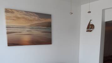 Una stanza con due sedie di legno con cuscini viola, un tavolo bianco, un quadro raffigurante una spiaggia e un lampadario.